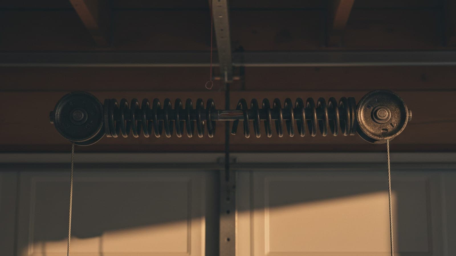 Close-up of a broken torsion spring mounted above a garage door with a visible gap in the coil where the spring snapped