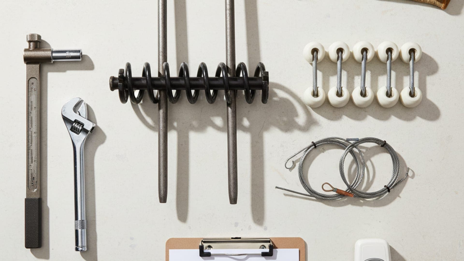 Overhead flat-lay of professional garage door service equipment including torsion springs, winding bars, cables, rollers, and tools on a clean work surface